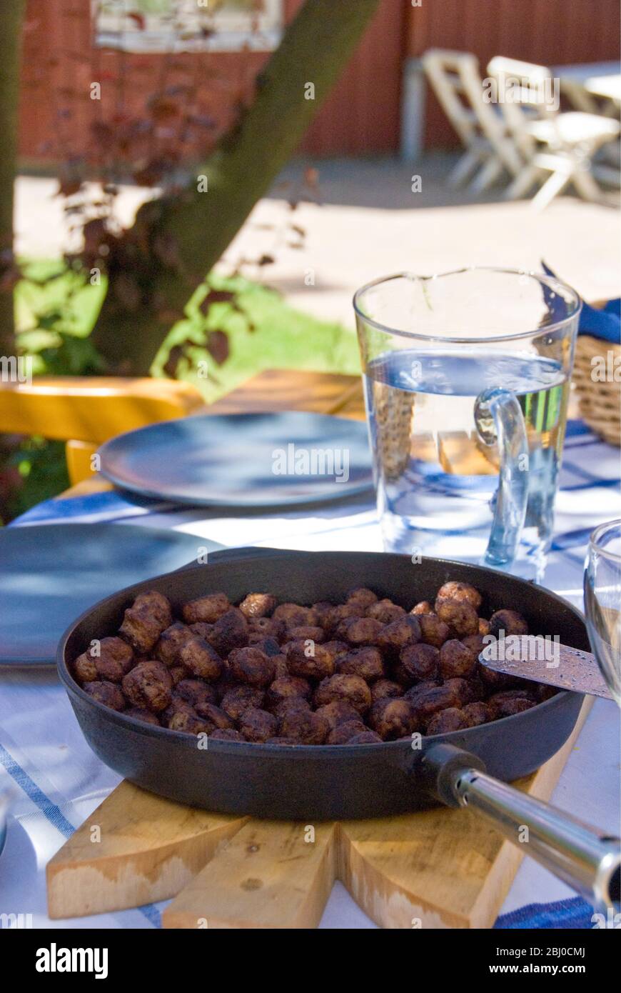 Frying pan of Swedish meatballs on table outside in dappled summer sunshine - Stock Photo