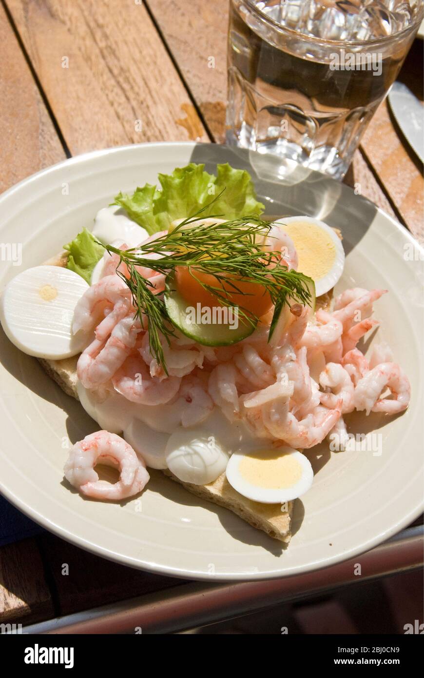 Swedish open sandwich of fresh prawns piled high on homemde flat bread with salad and mayonnaise, served on cafe table outdoors - Stock Photo
