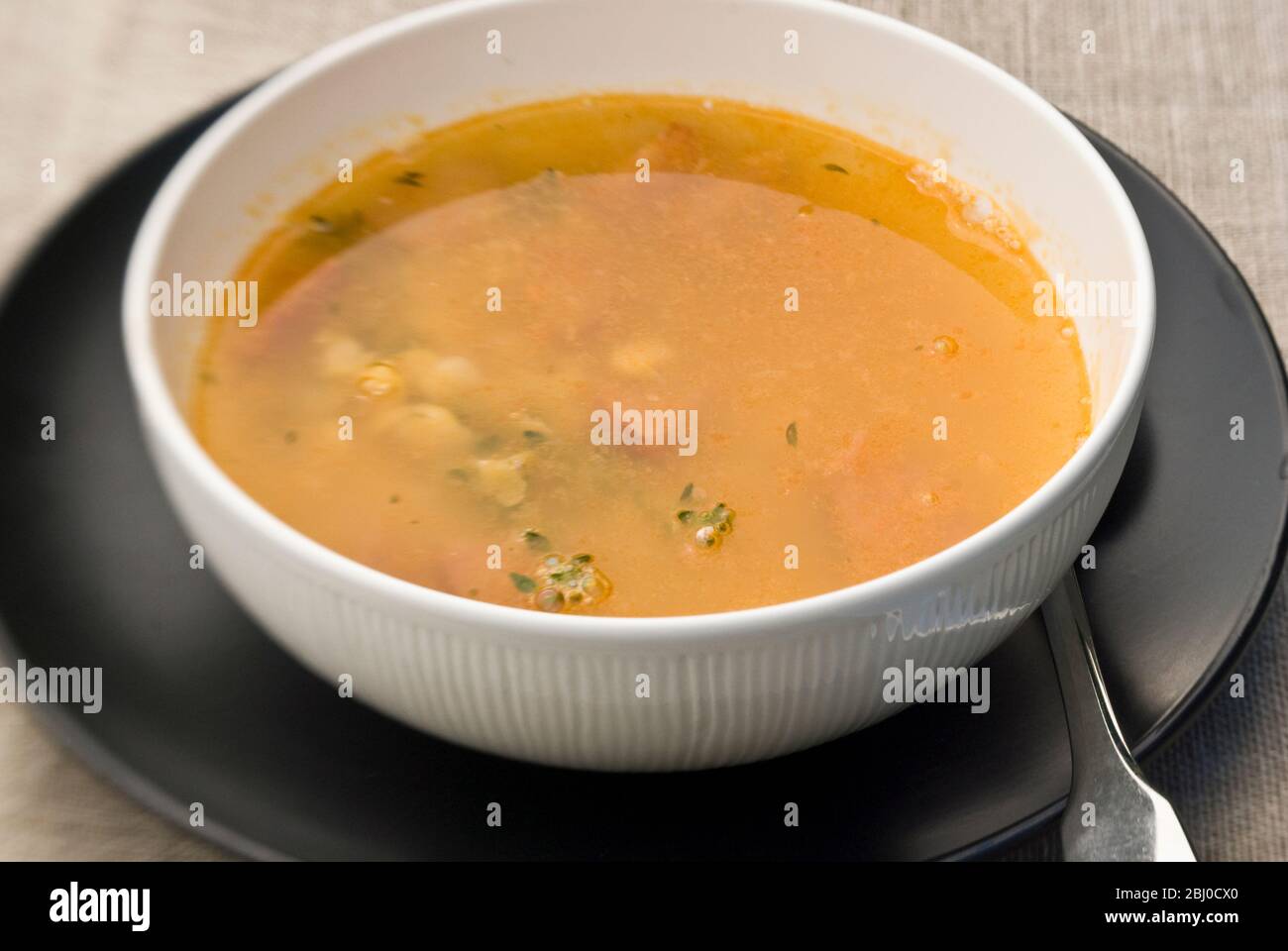 Bowl of warming soup made of yellow split peas, good stock, pieces of chorizo sausage, and thyme sprigs - Stock Photo