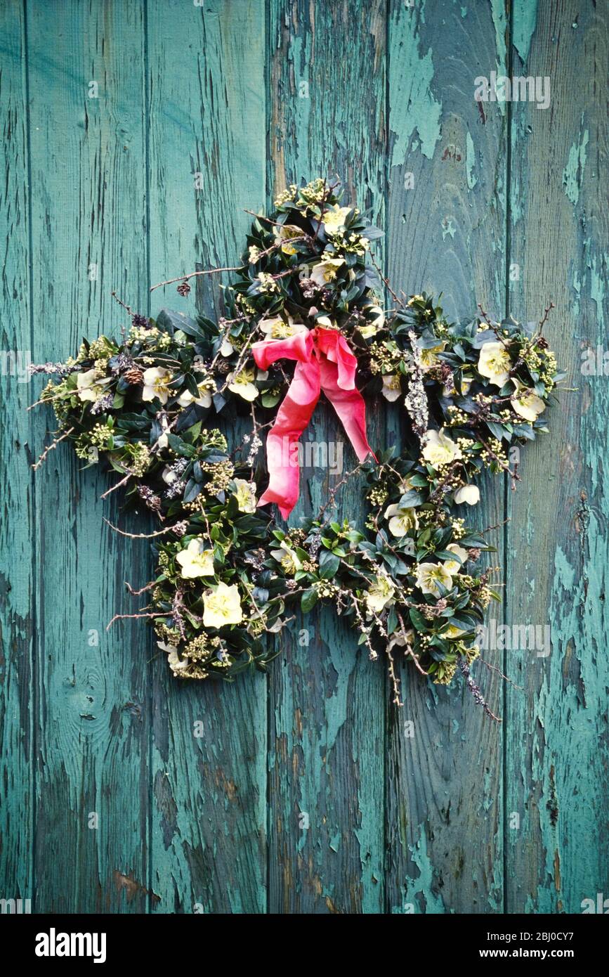 Star shaped wreath made on bent wore coat hangers, hanging on old peeling green door with red ribbon - Stock Photo