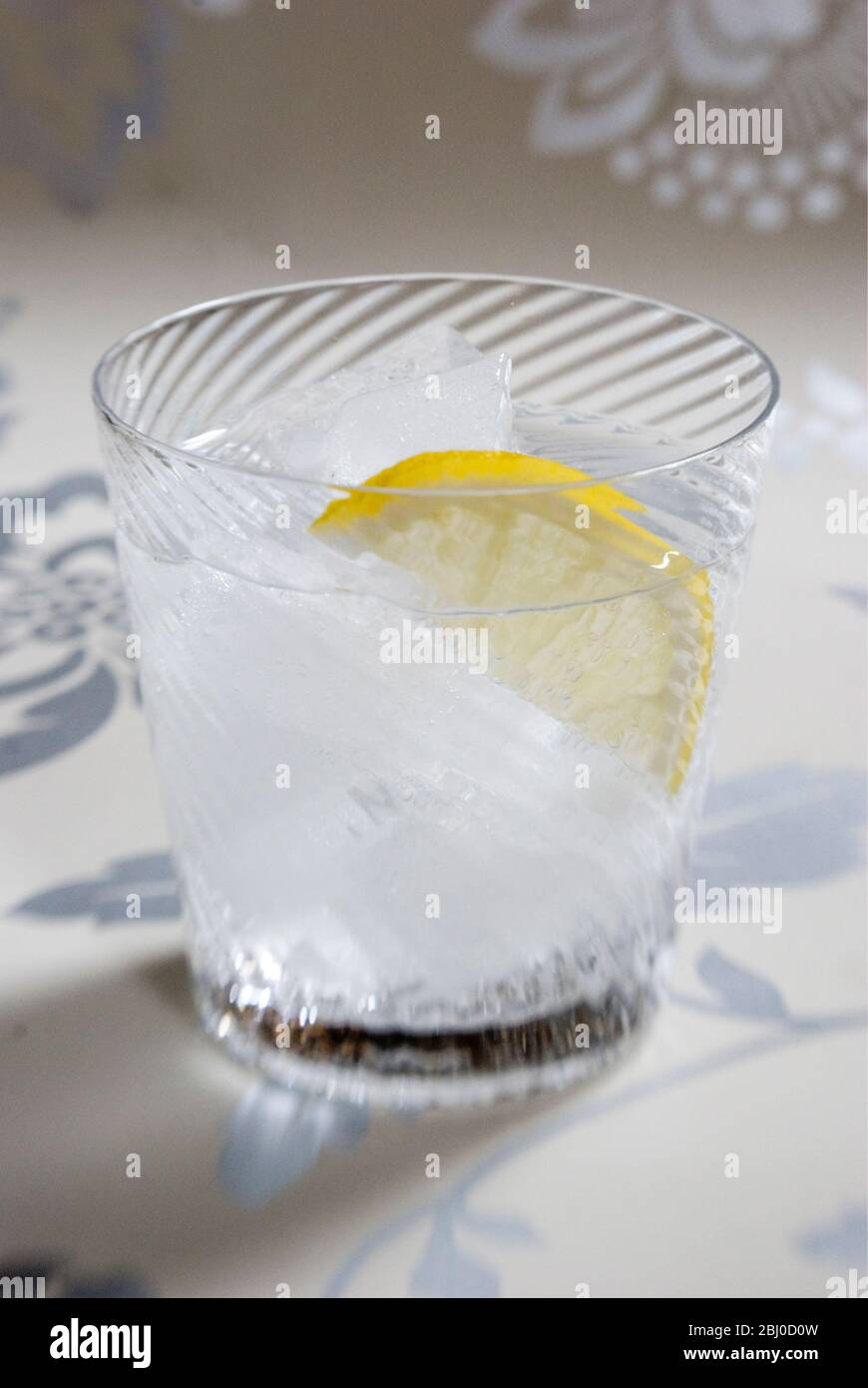 Fine spiral blown glass of clear spirit with soda or tonic, and slice of lemon on decorative background - Stock Photo