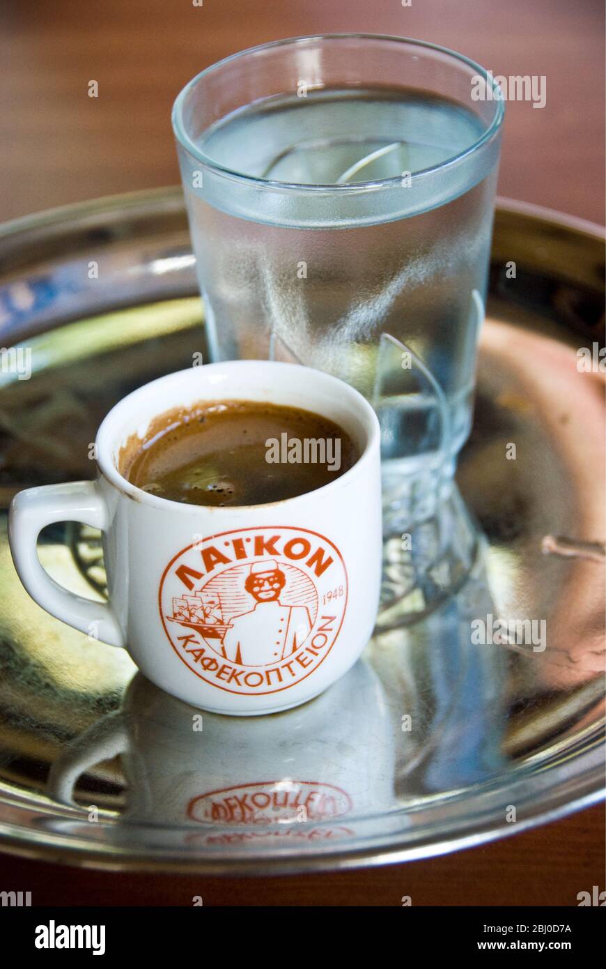Little cup of strong Greek coffee, with glass of water on tray on table of hillside restaurant in southern Cyprus - Stock Photo