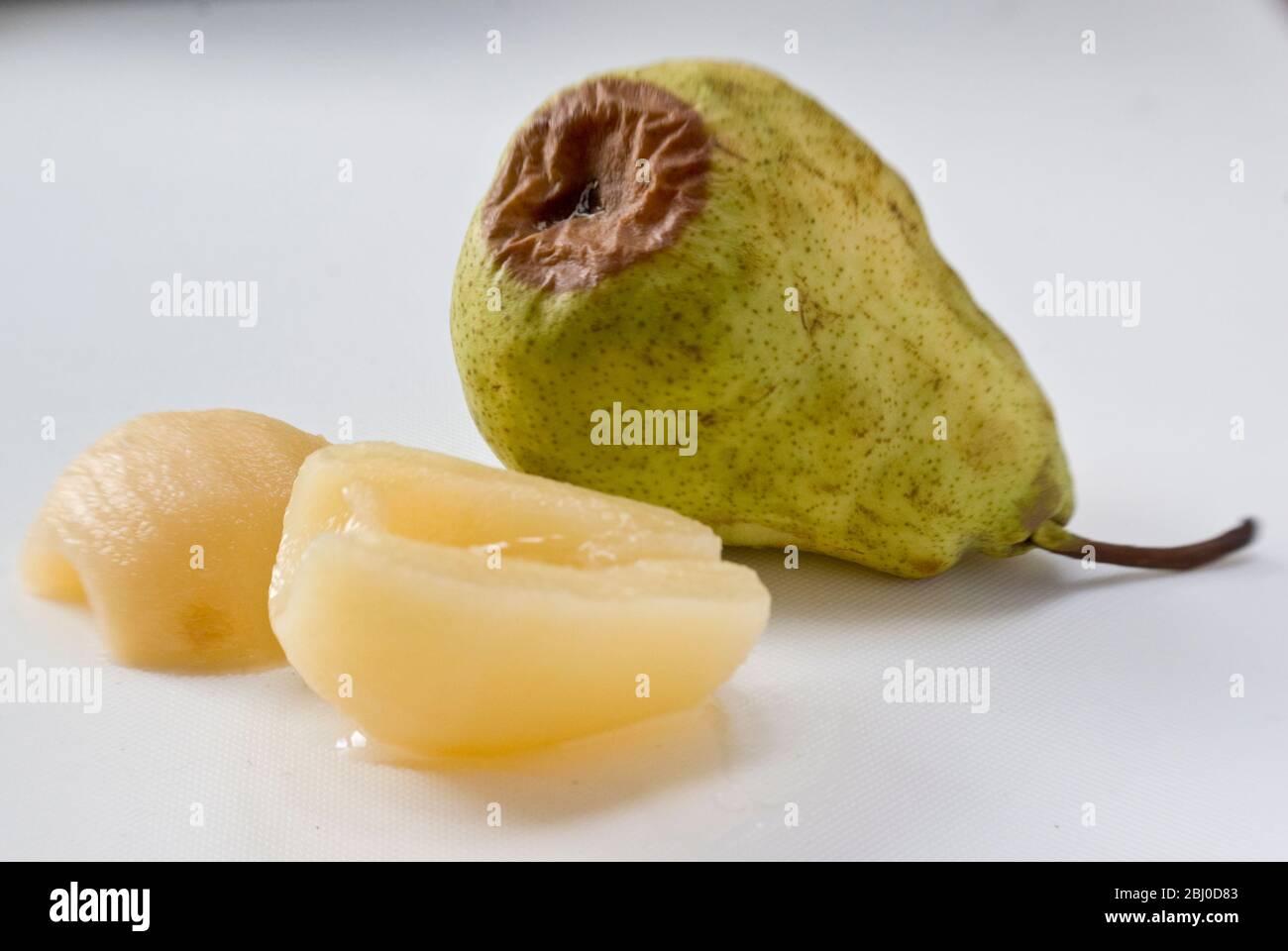 Comparison of fresh, raw pear, starting to rot with canned pears showing the advantage of tinned fruit. - Stock Photo