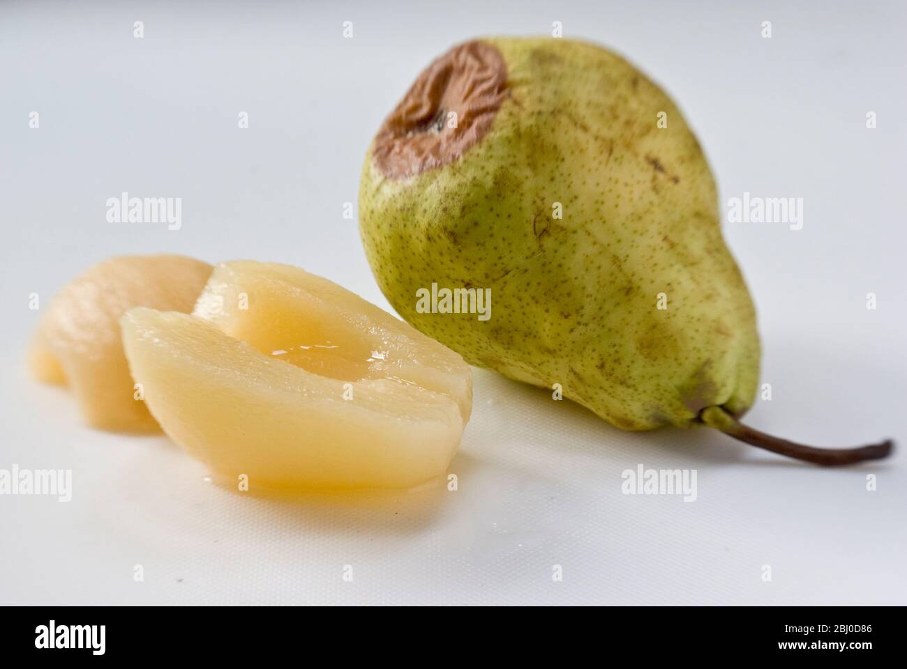 Comparison of fresh, raw pear, starting to rot with canned pears showing the advantage of tinned fruit. - Stock Photo