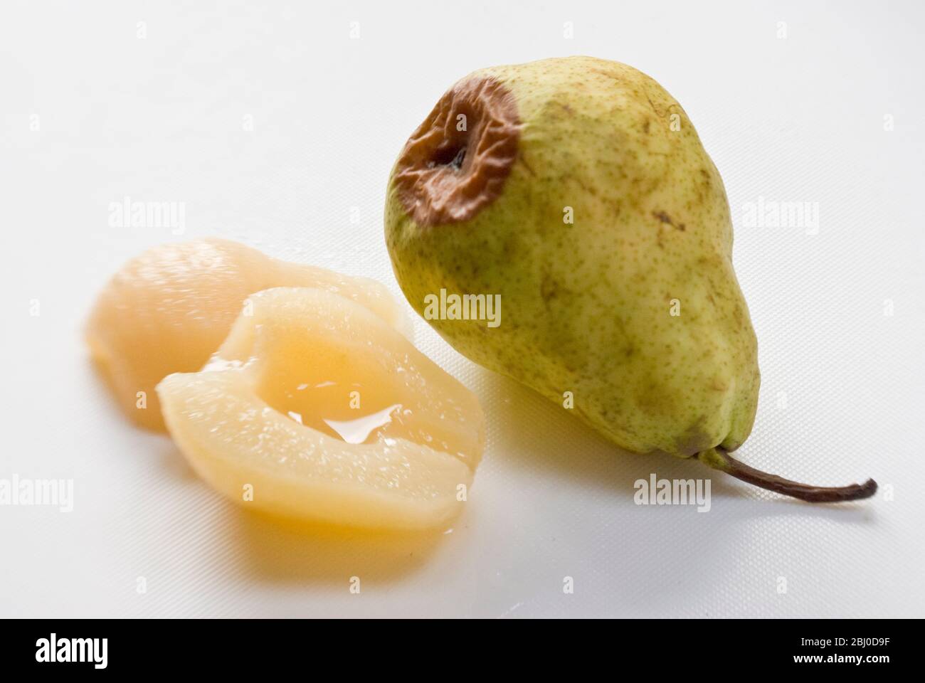 Comparison of fresh, raw pear, starting to rot with canned pears showing the advantage of tinned fruit. - Stock Photo