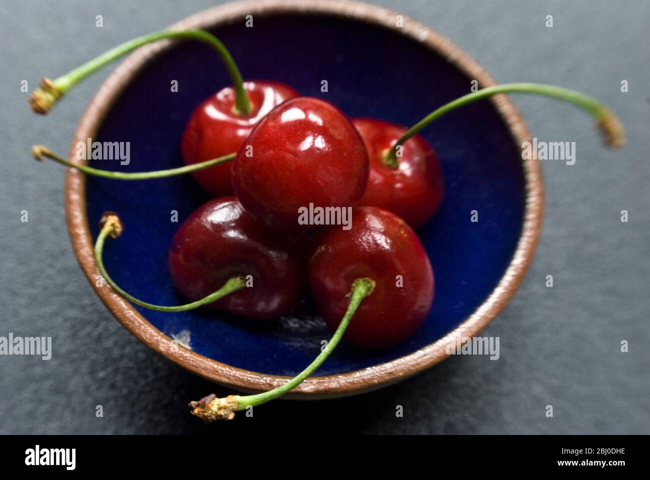 Red cherries on small blue pottery bowl - Stock Photo
