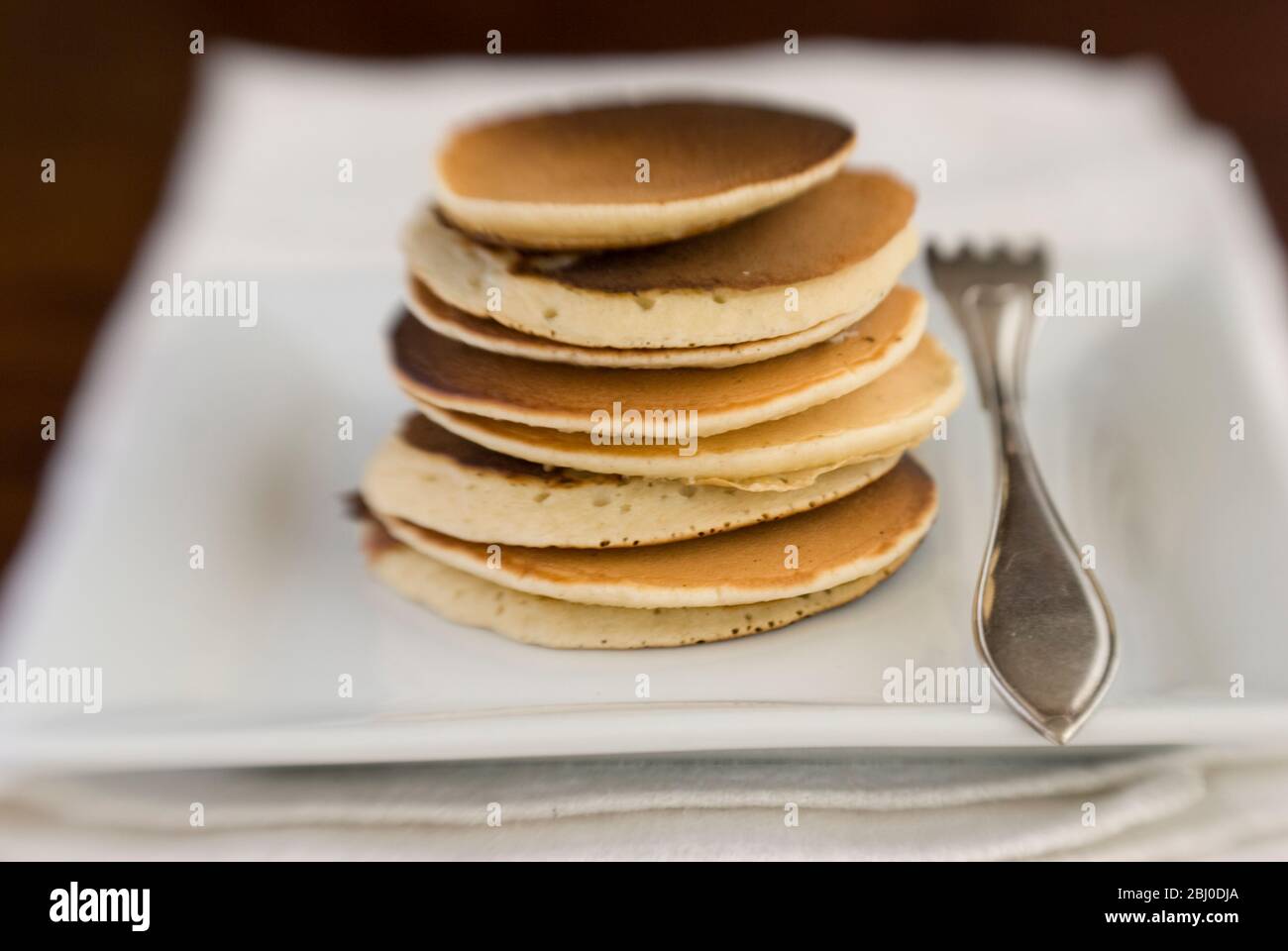 Stack of Scotch pancakes on white plate with silver fork - Stock Photo