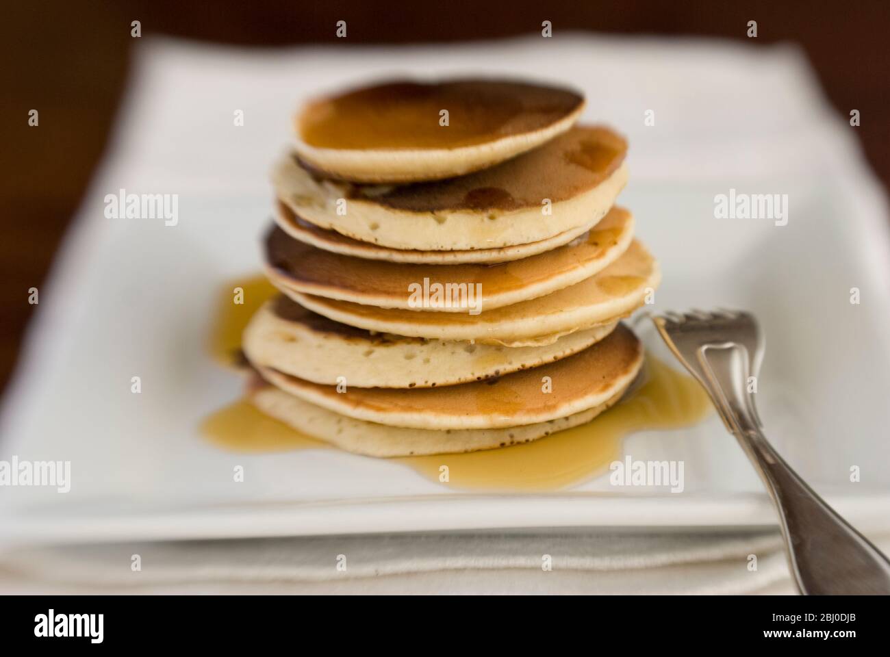 Stack of Scotch pancakes on white plate with silver fork and maple syrup - Stock Photo