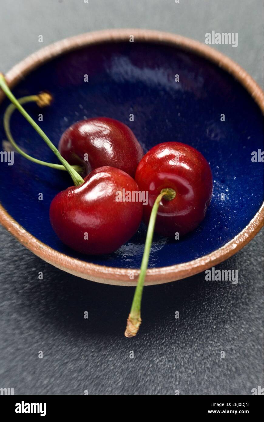 Red cherries on small blue pottery bowl - Stock Photo