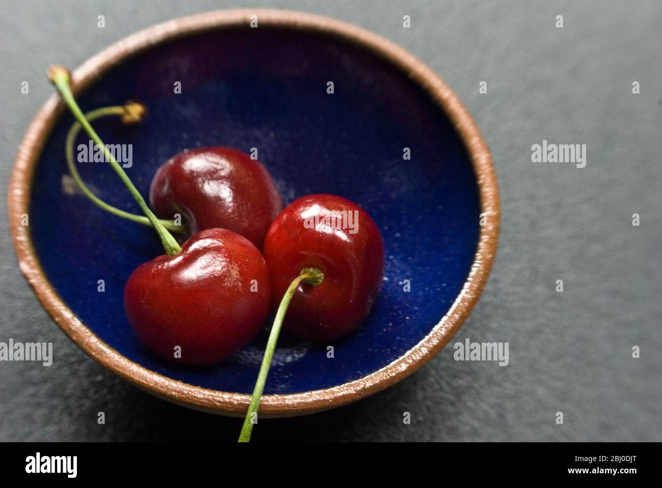 Red cherries on small blue pottery bowl - Stock Photo