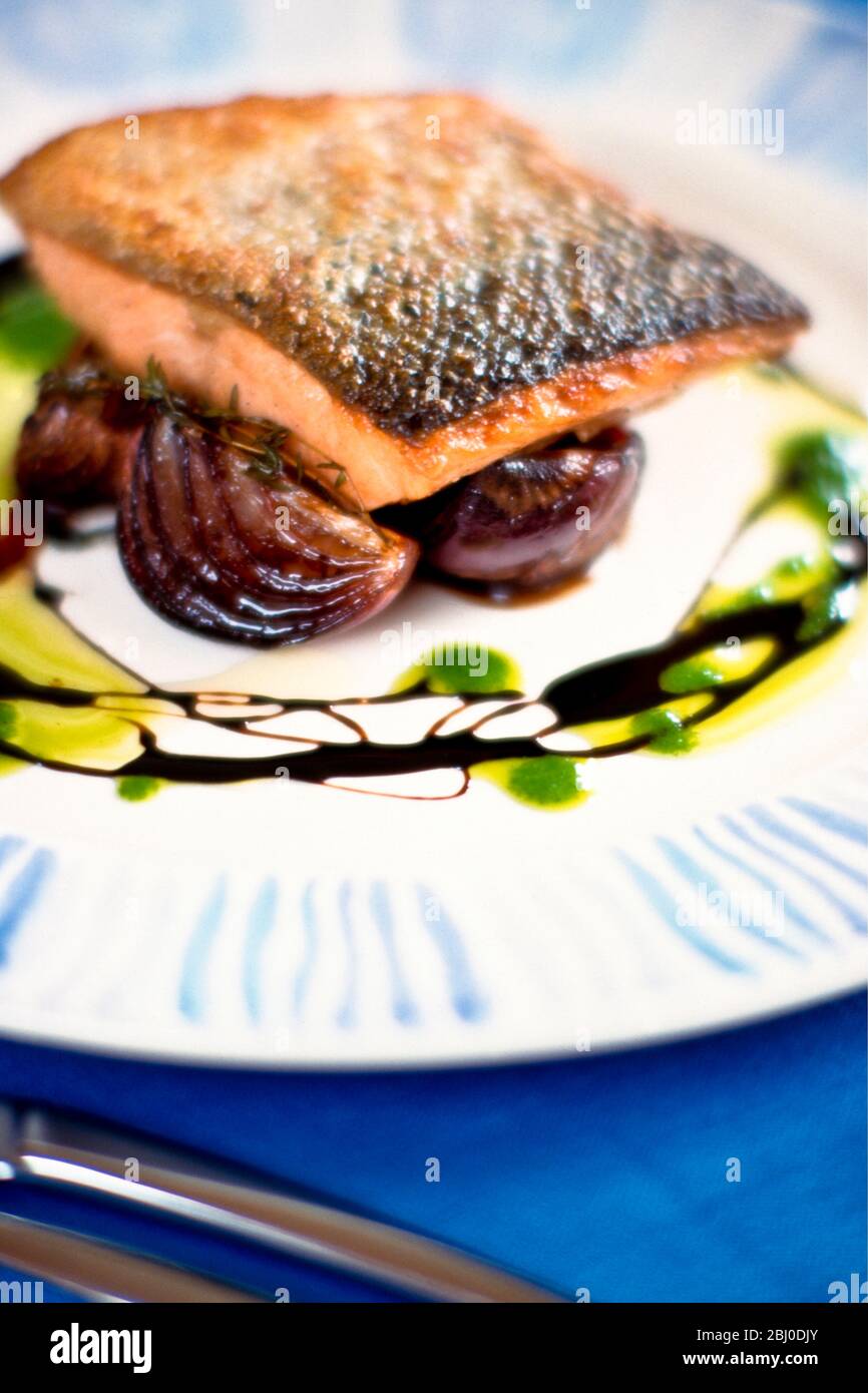 Pan fried salmon fillet on caramelised red onions with balsamic vinegar and thin pesto sauce run round plate. - Stock Photo