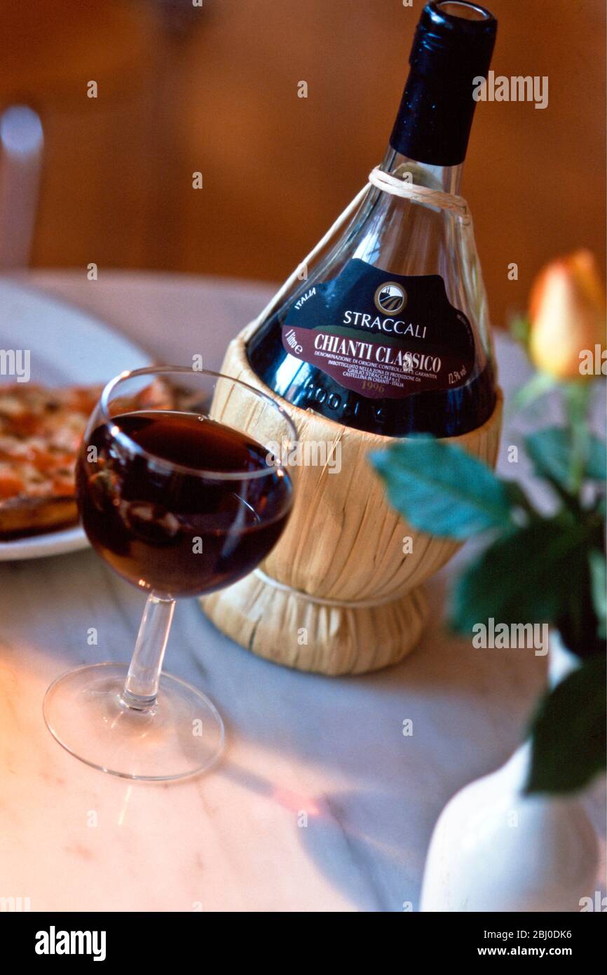 Chianti classico in traditional old fashioned raffia covered bbottle on restaurant table with pizza - Stock Photo