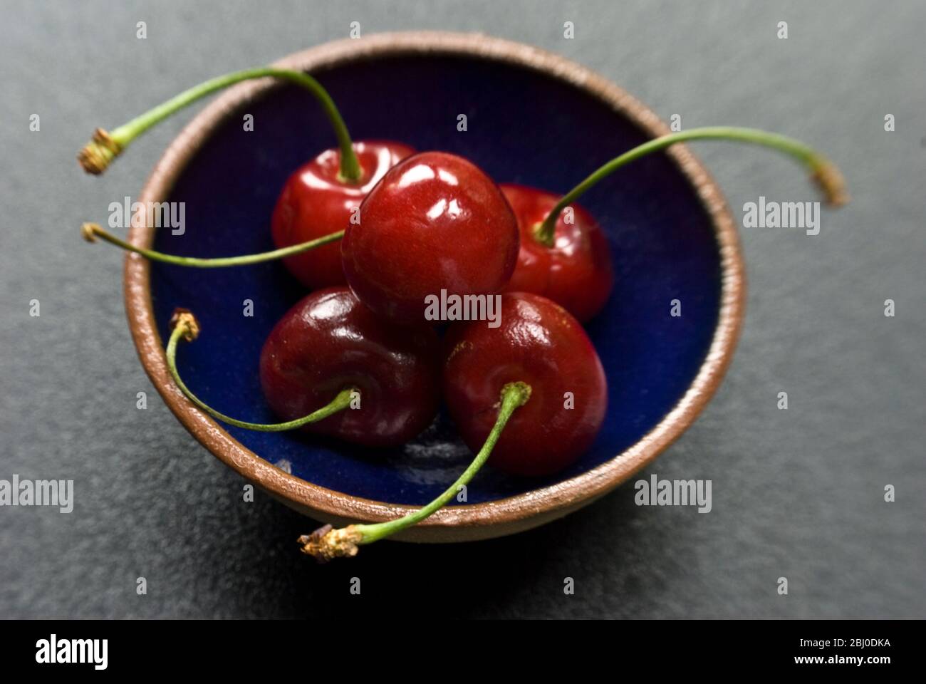 Red cherries on small blue pottery bowl - Stock Photo