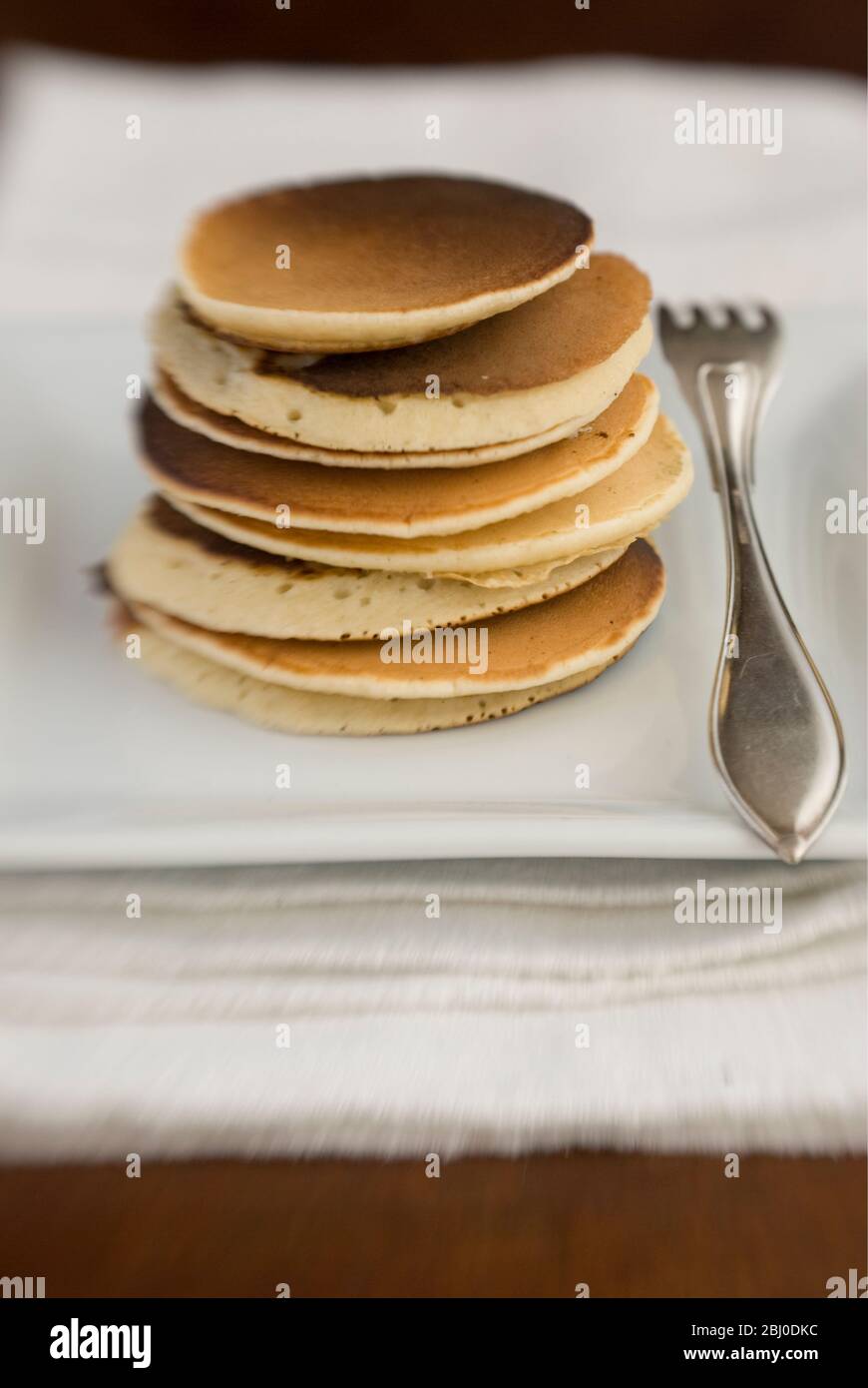 Stack of Scotch pancakes on white plate with silver fork - Stock Photo