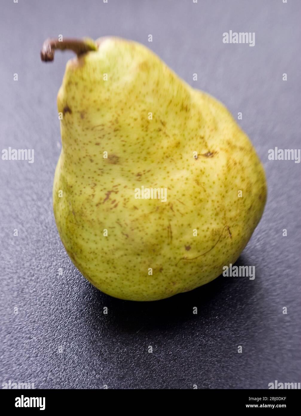 Single yellow green pear on dark surface. - Stock Photo