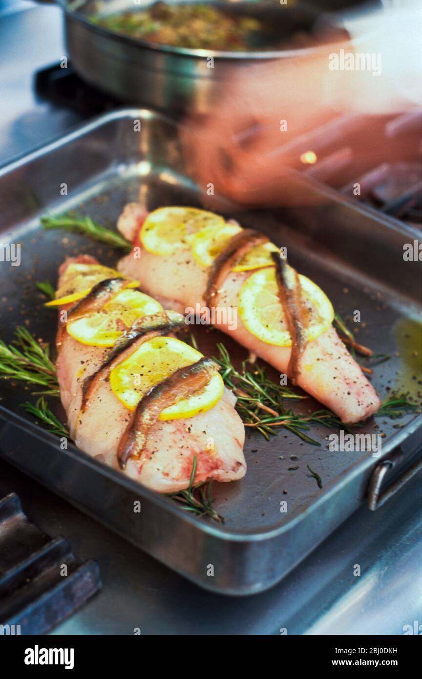 Fillets of monkfish in pan ready to be roasted on bed of rosemary with lemon and anchovies - Stock Photo