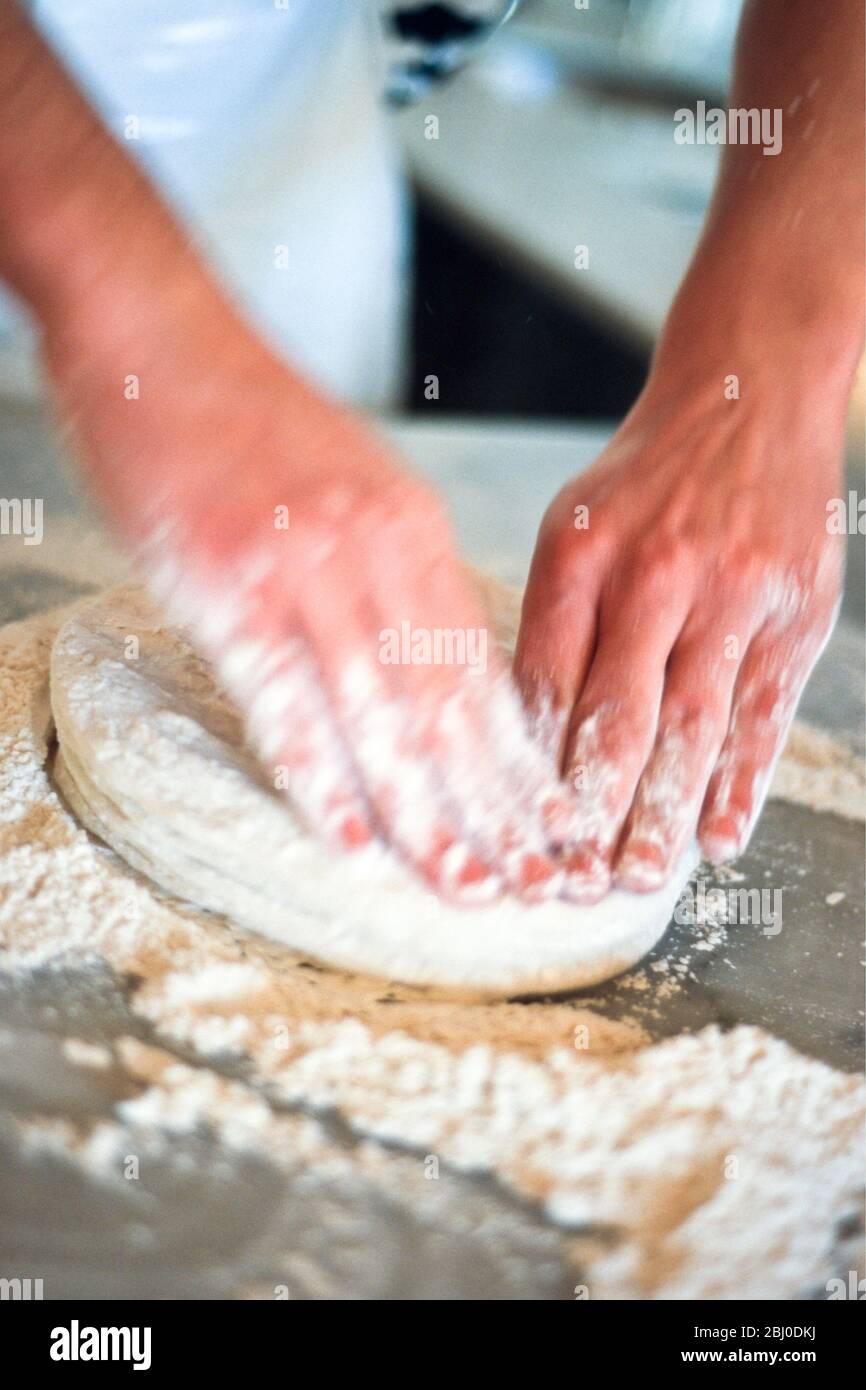 Kneading pizza dough on stainless steel surface. - Stock Photo