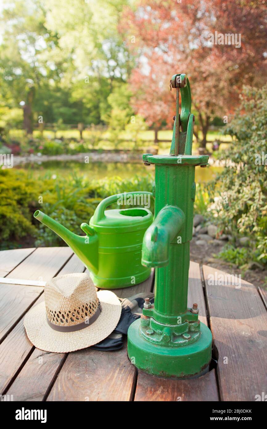 Green water pump with watering can in a sunny garden focus on the