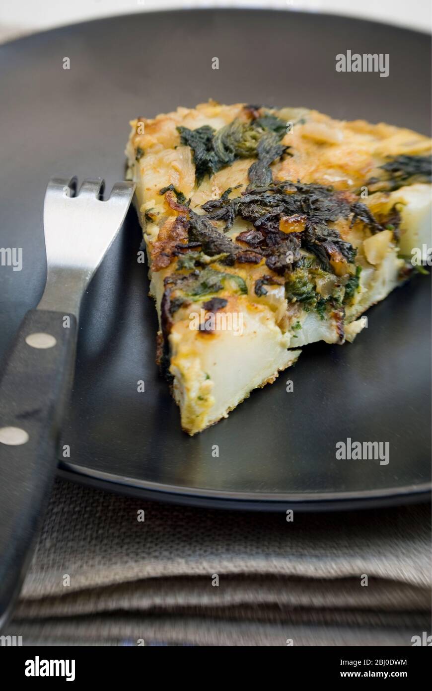 Slice of Spanish tortilla made with potatoes, onions, eggs and freshly picked springtime nettle tops - Stock Photo