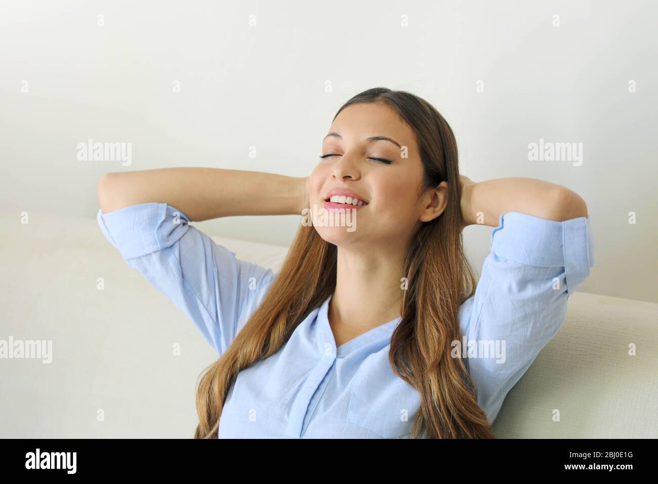 Portrait of a young smiling woman relaxing with closed eyes on a sofa after work at home relaxing breathing fresh air sit on comfortable couch in livi Stock Photo