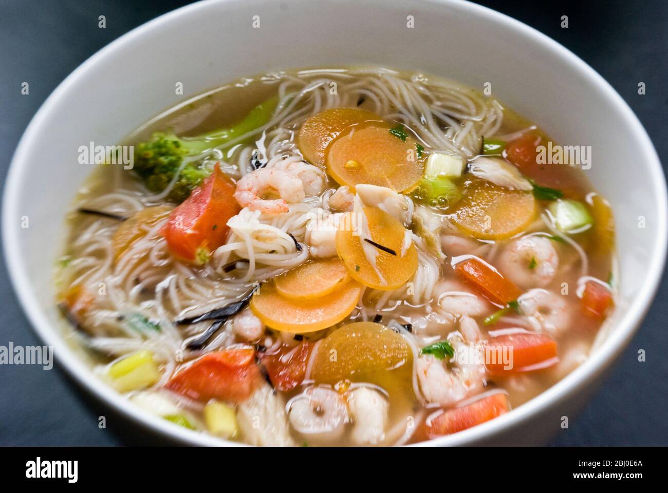 Bowl of asian style soup with rice noodles, prawns, and vegetables - Stock Photo