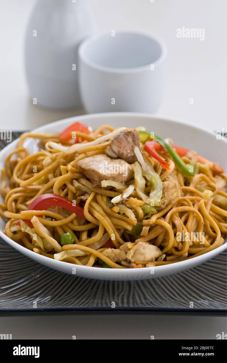 Stir-fried ramen-style noodles with pieces of chicken, red peppers, bean sprouts, onions and carrots and flavoured with sosu, salt and pepper. - Stock Photo