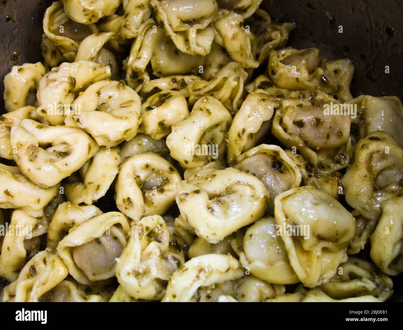 Close up of cooked tortelloni pasta tossed in pesto sauce in the pan - Stock Photo