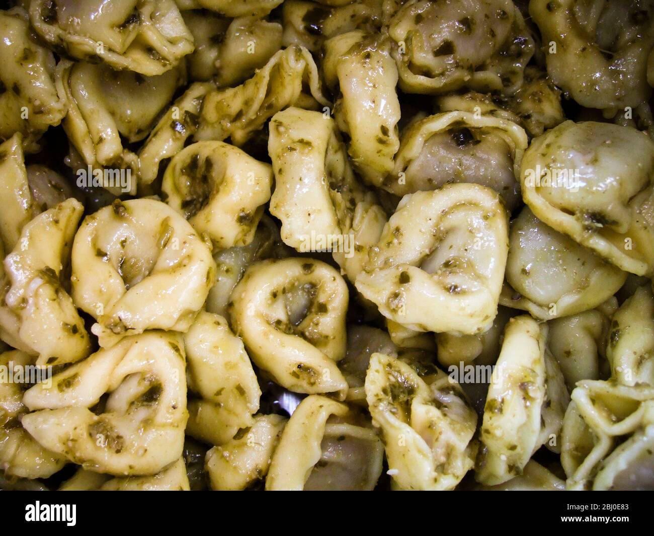 Close up of cooked tortelloni pasta tossed in pesto sauce in the pan - Stock Photo