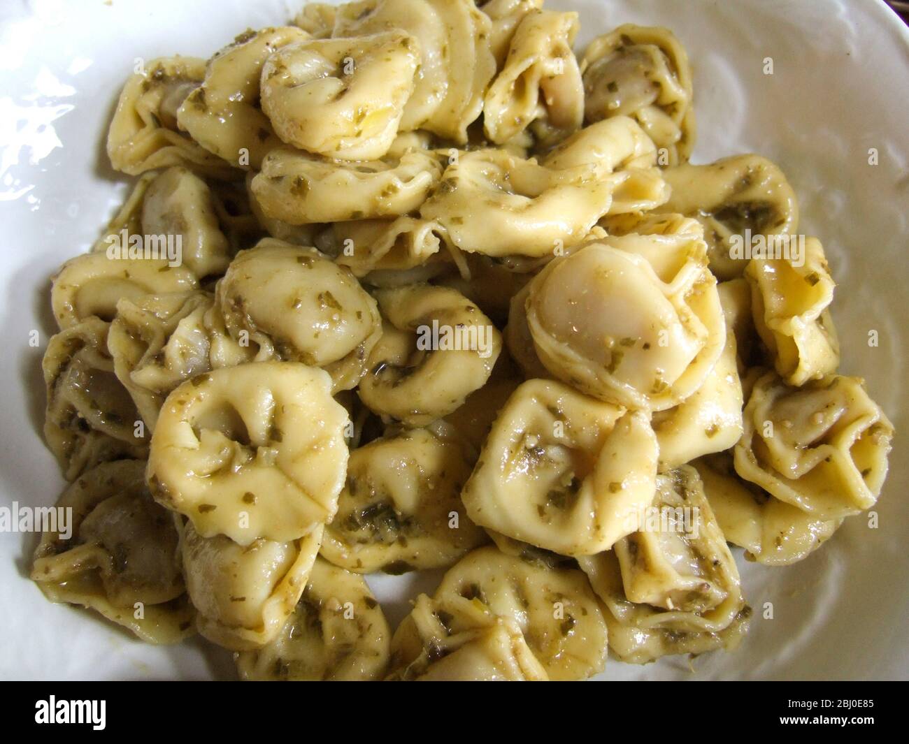 Close up of cooked tortelloni pasta tossed in pesto sauce on a white plate - Stock Photo