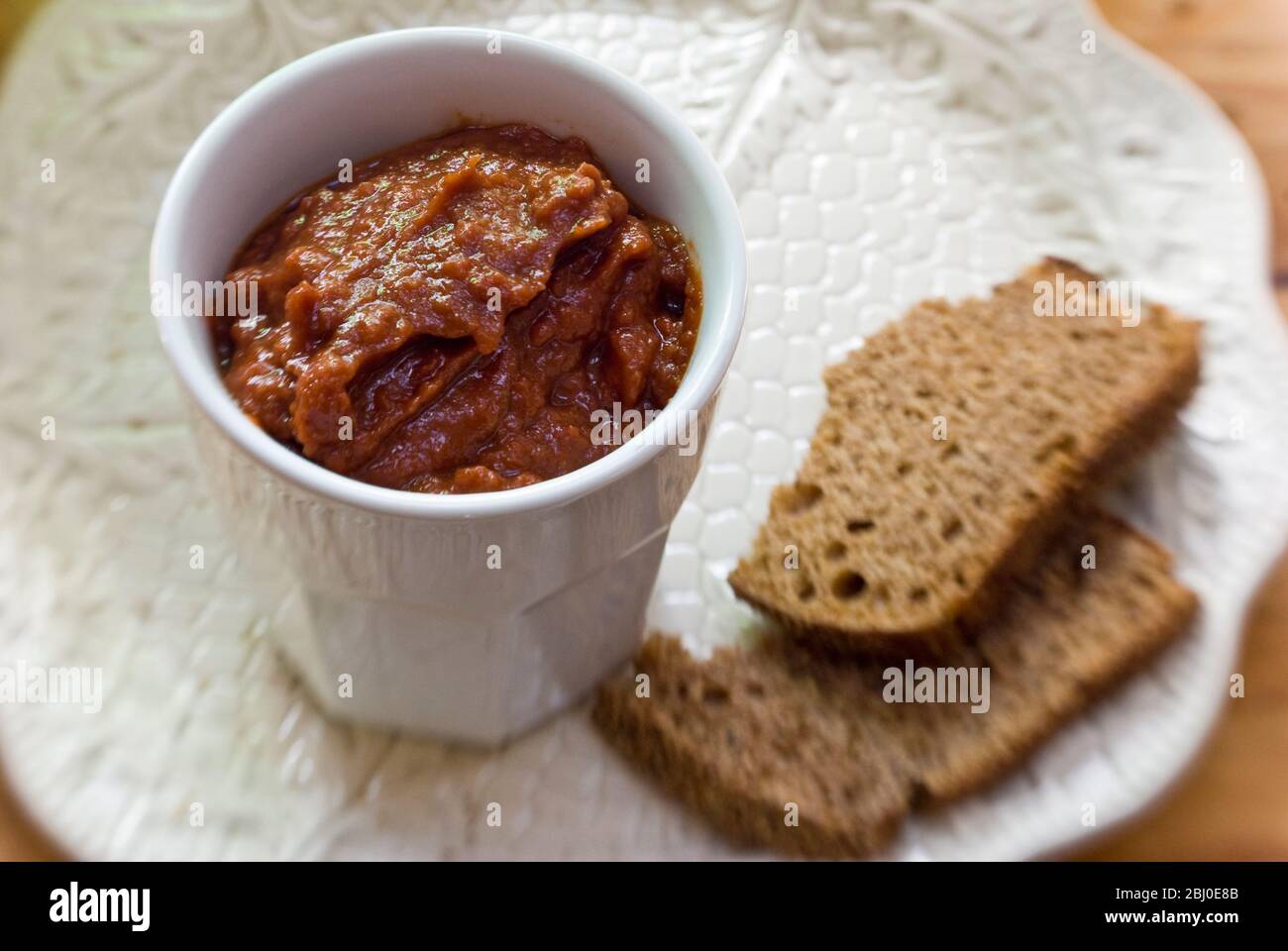 White pot of sundried tomato pate as dip with coarse rye bread. - Stock Photo