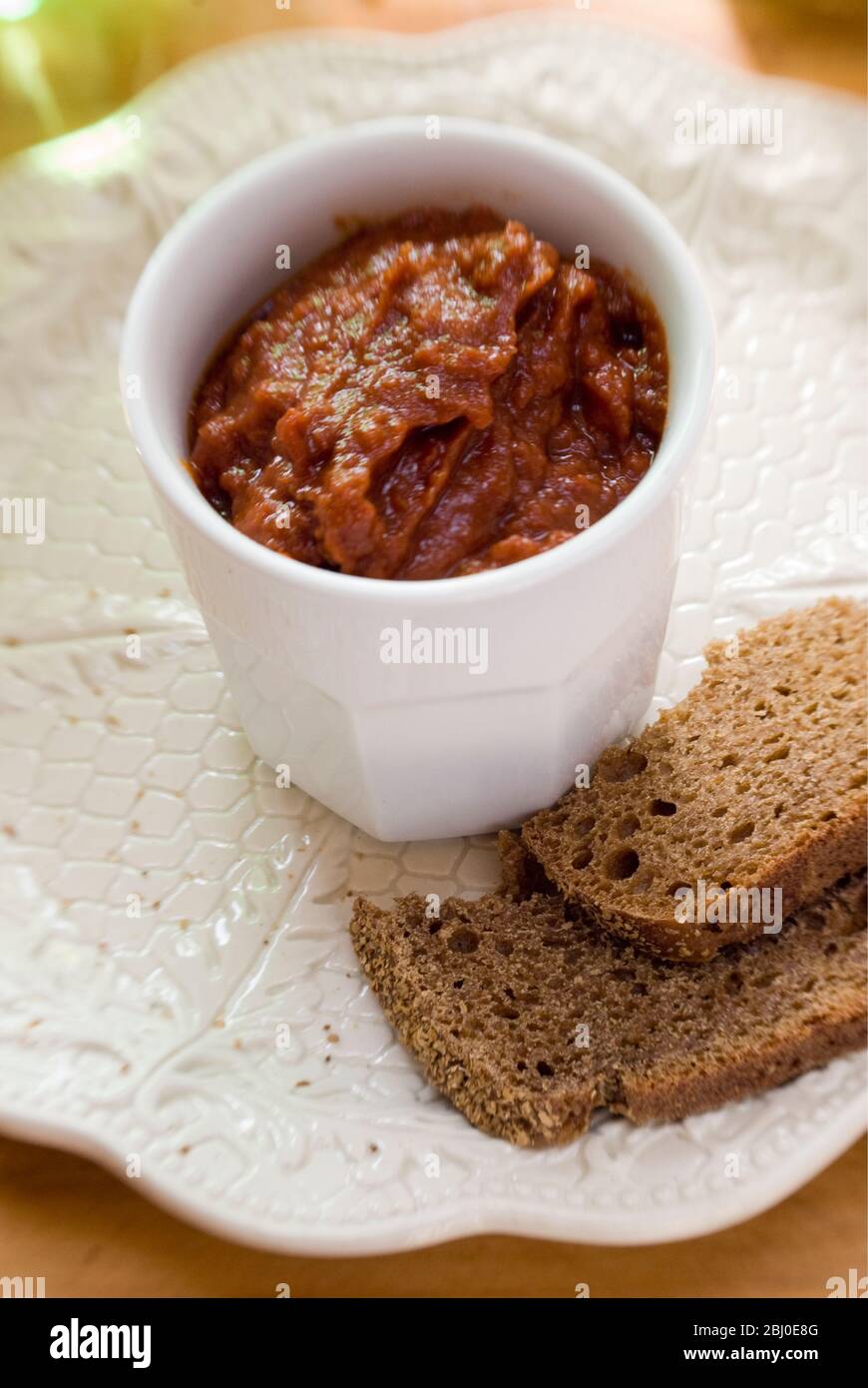 White pot of sundried tomato pate as dip with coarse rye bread. - Stock Photo
