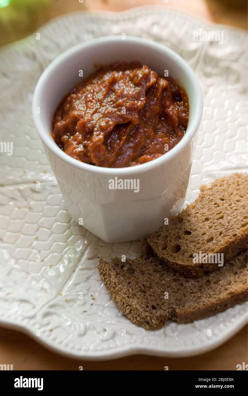 White pot of sundried tomato pate as dip with coarse rye bread. - Stock Photo