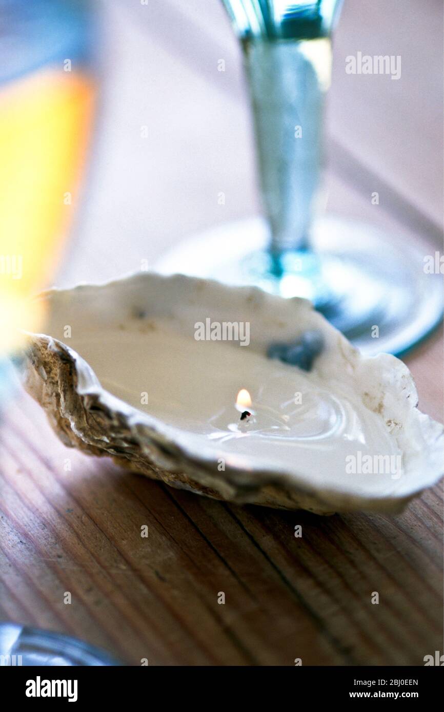 Oyster shell filled with candle wax with wick as part of table decoration - Stock Photo
