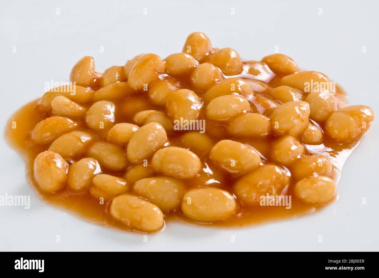 Small heap of baked beans in tomato sauce on white surface - Stock Photo