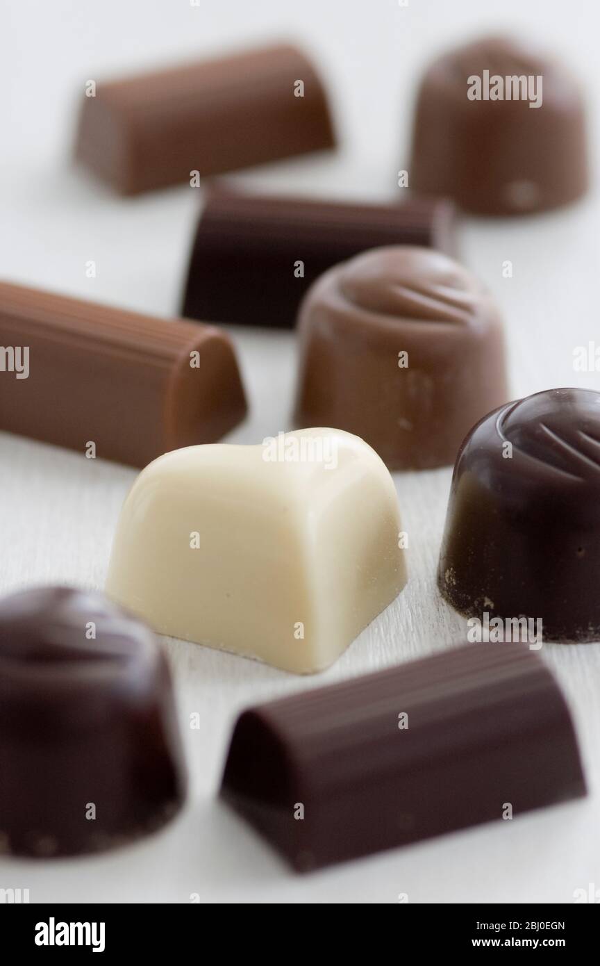 A selection of white, dark, and milk chocolates on white surface. - Stock Photo