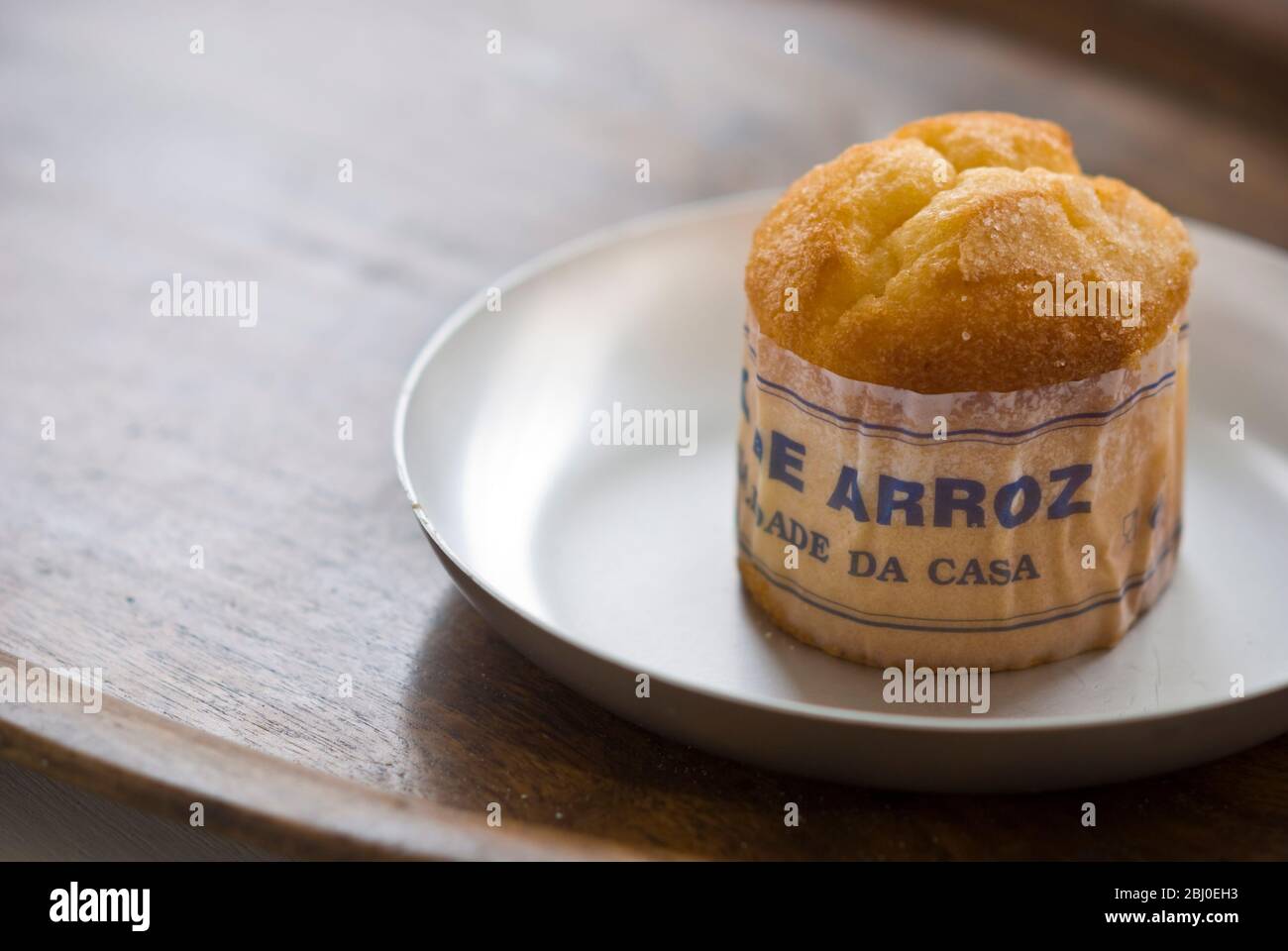 Classic Portuguese muffin type cake made with rice in paper wrapper on metal plate, with cup of black coffee - Stock Photo