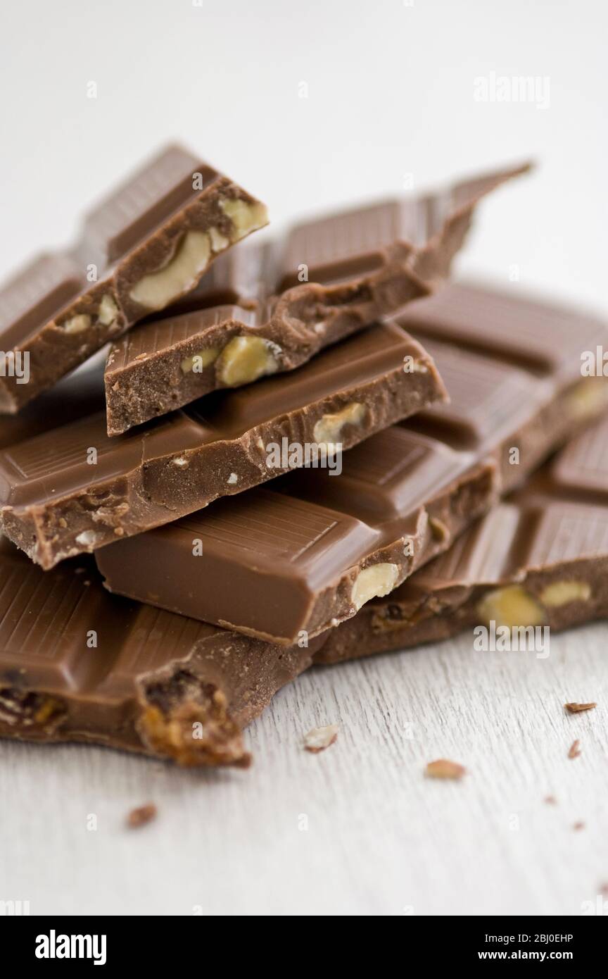 Pile of broken pieces of nut mik chocolate bar on white surface. - Stock Photo