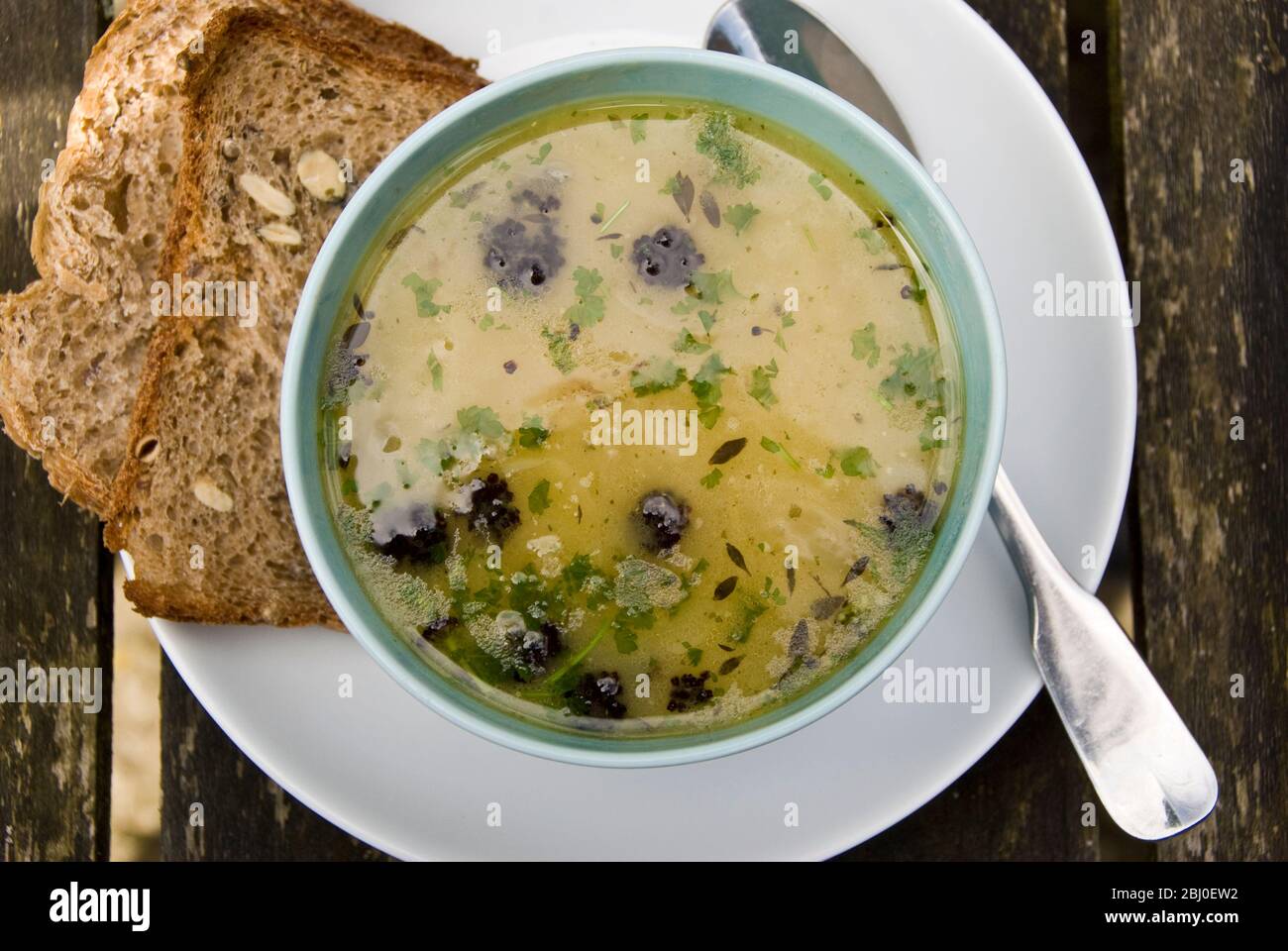 Bowl of chicken soup with Cypriot trahanas, purple sprouting broccoli and chopped parsley, with wholemeal seeded rye bread on the side. - Stock Photo