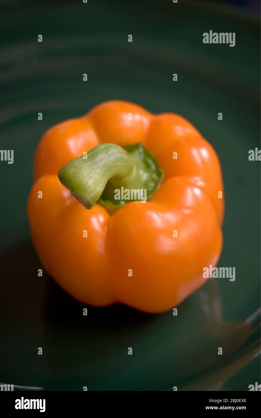 Orange pepper on dark green plate - Stock Photo