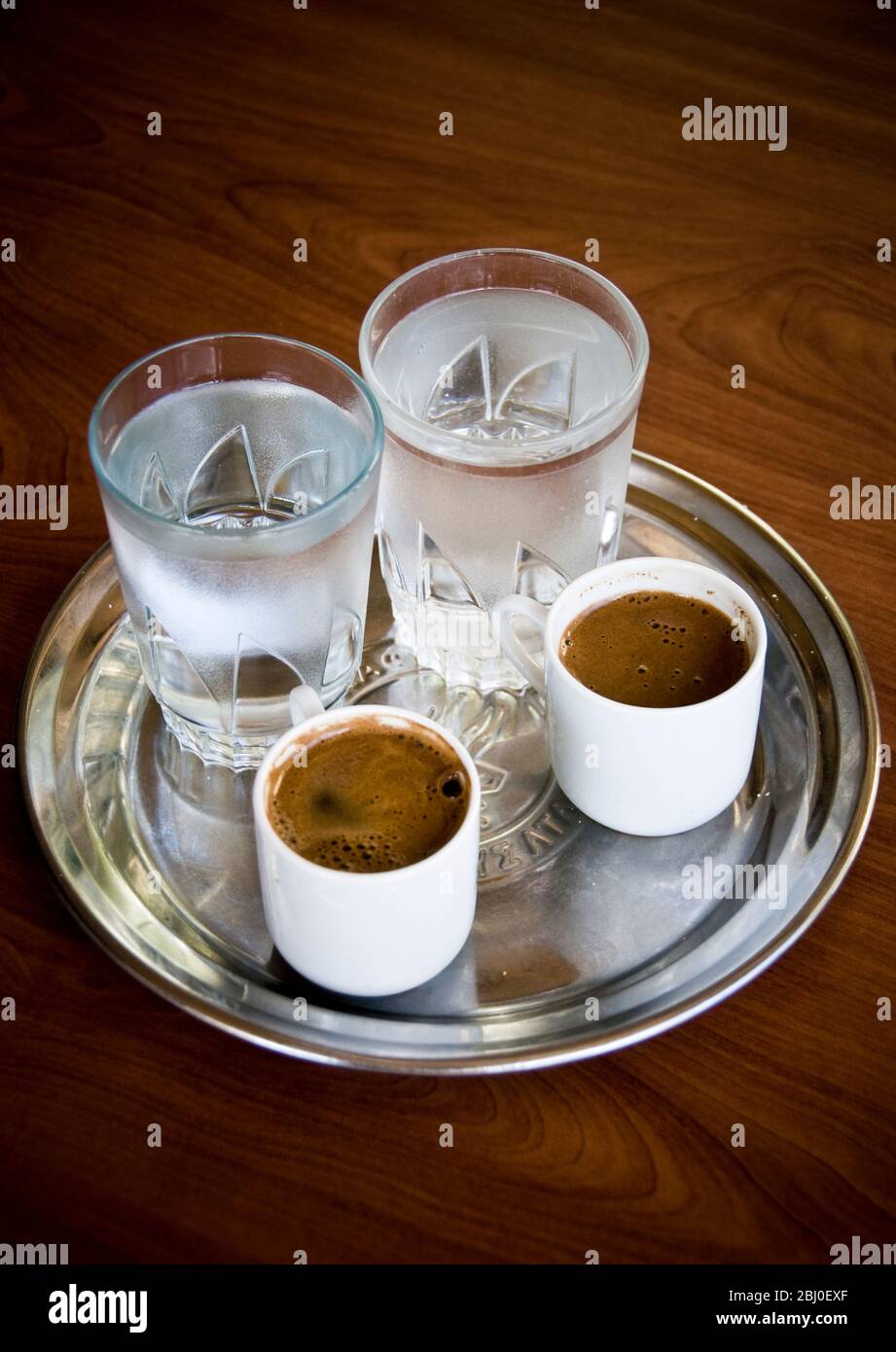 Two little cups of Greek coffee with accompanying glasses of water served in Cypriot cafe in the hills in southern Cyprus - Stock Photo