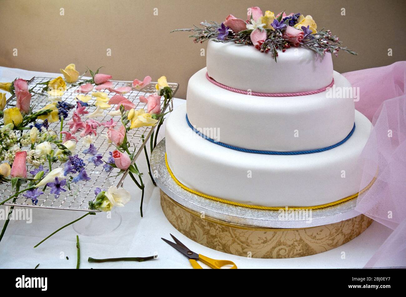 Wedding or celebration cake, decorated with sugar frosted flowers and pastel cords. - Stock Photo