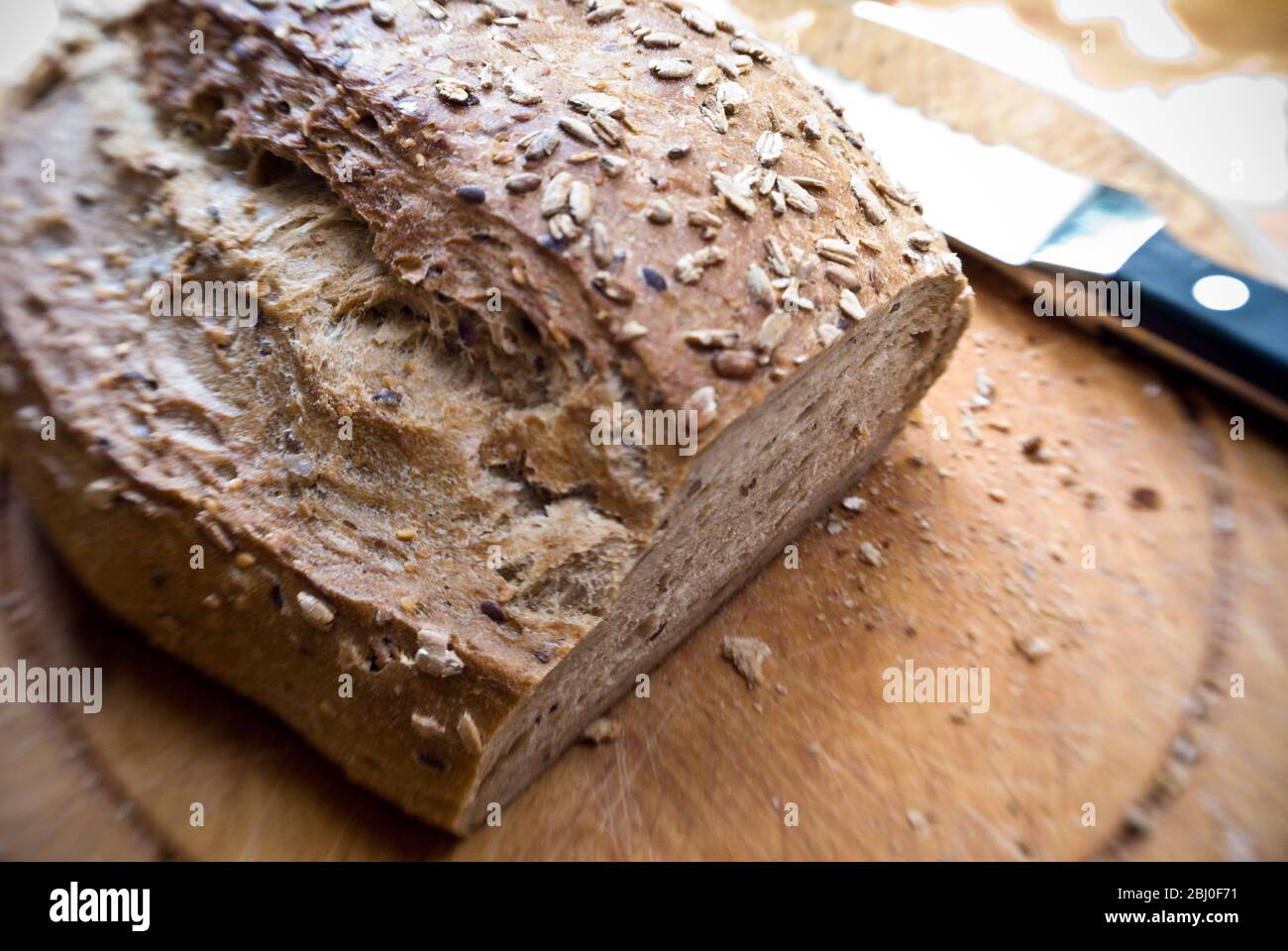 Slicing a wholegrain, rye and walnut loaf on old wooden board. - Stock Photo