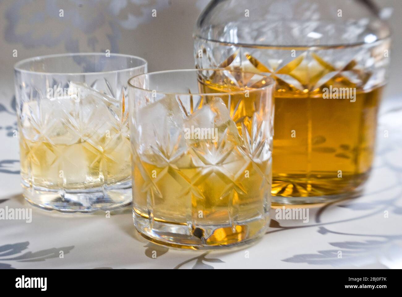 Scotch whisky on ice in cut lead crystal glasses on decorative silver surface, with decanter