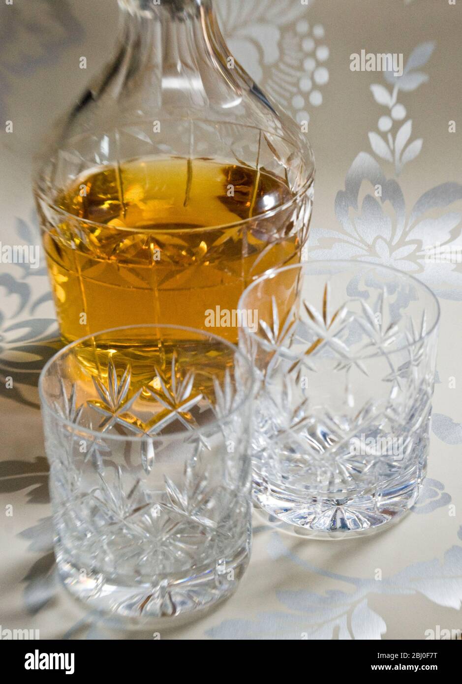 Scotch whisky on ice in cut lead crystal glasses on decorative silver surface, with decanter. - Stock Photo