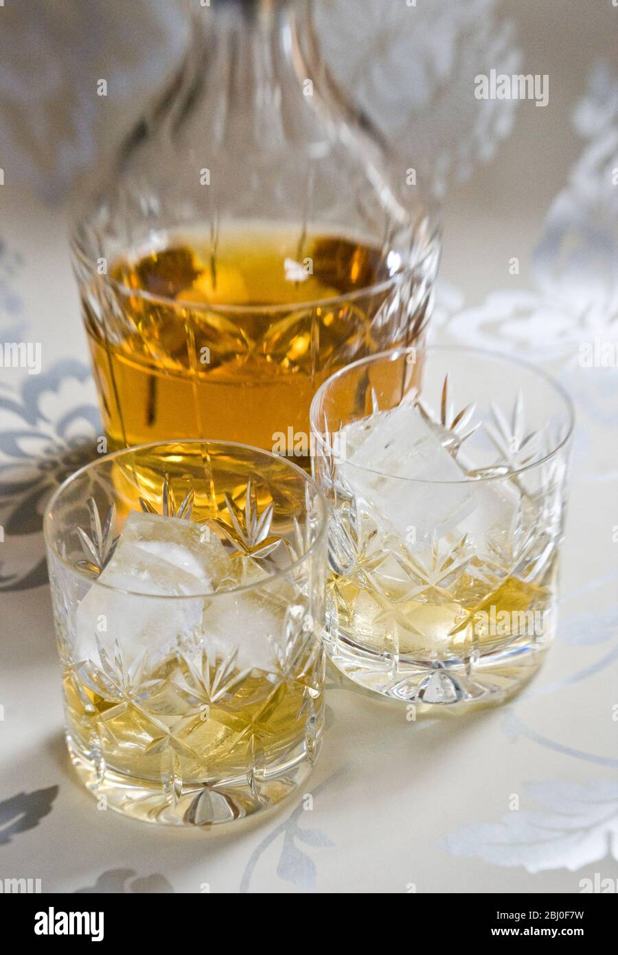 Scotch whisky on ice in cut lead crystal glasses on decorative silver surface, with decanter. - Stock Photo