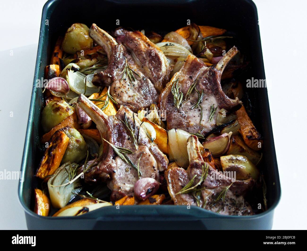 Roast pork chops with mixed roast vegetables seasoned with black pepper and fresh rosemary sprigs. - Stock Photo