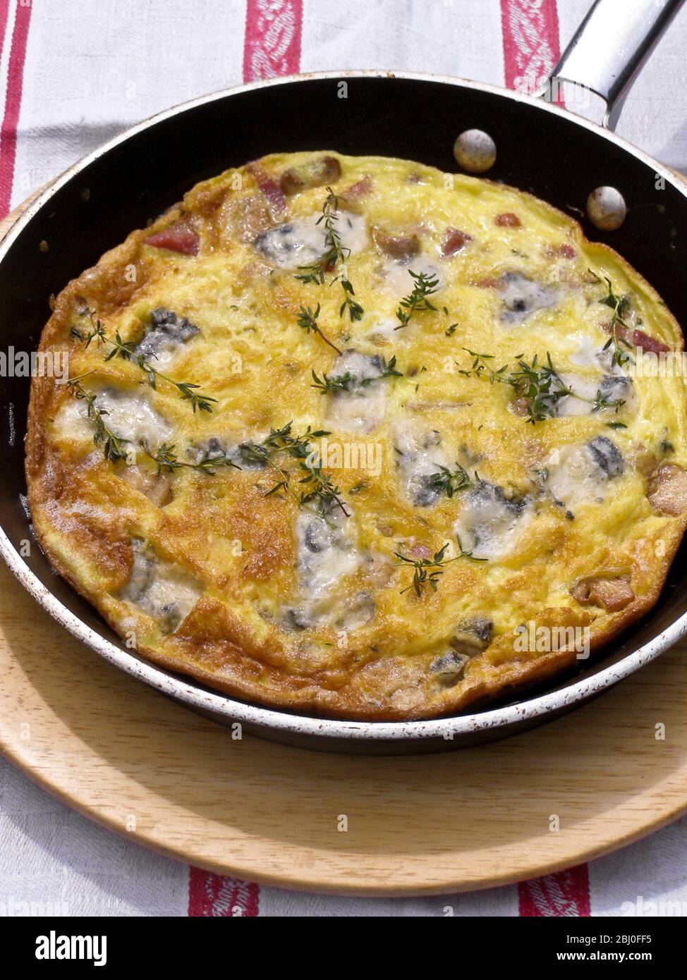 Frittata with goat's cheese, mushrooms and thyme, served in frying pan on wooden plate. - Stock Photo