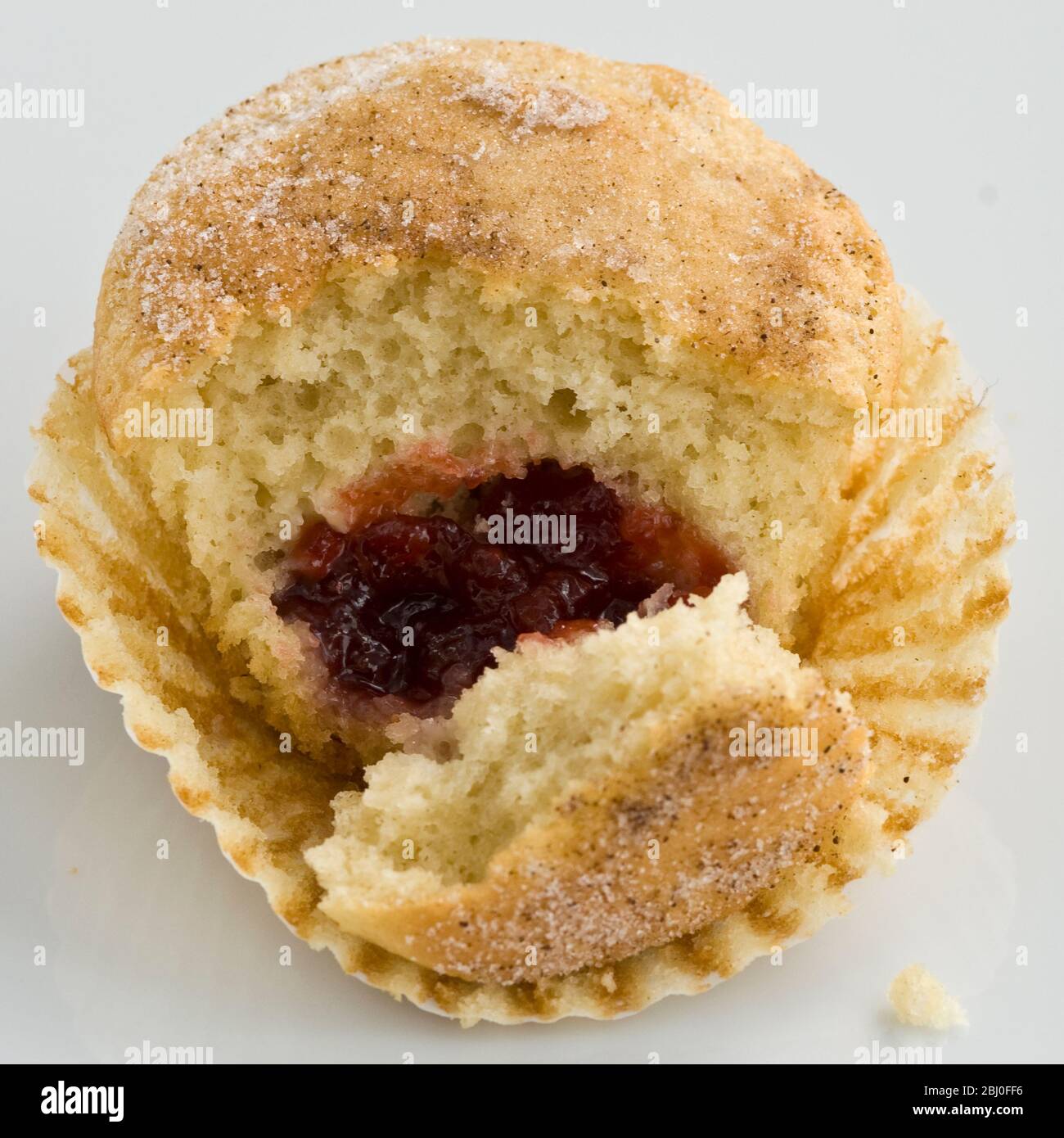 Muffin with sugary top filled with jam (jelly), broken open to show filling. A muffin masqerading as a doughnut! - Stock Photo