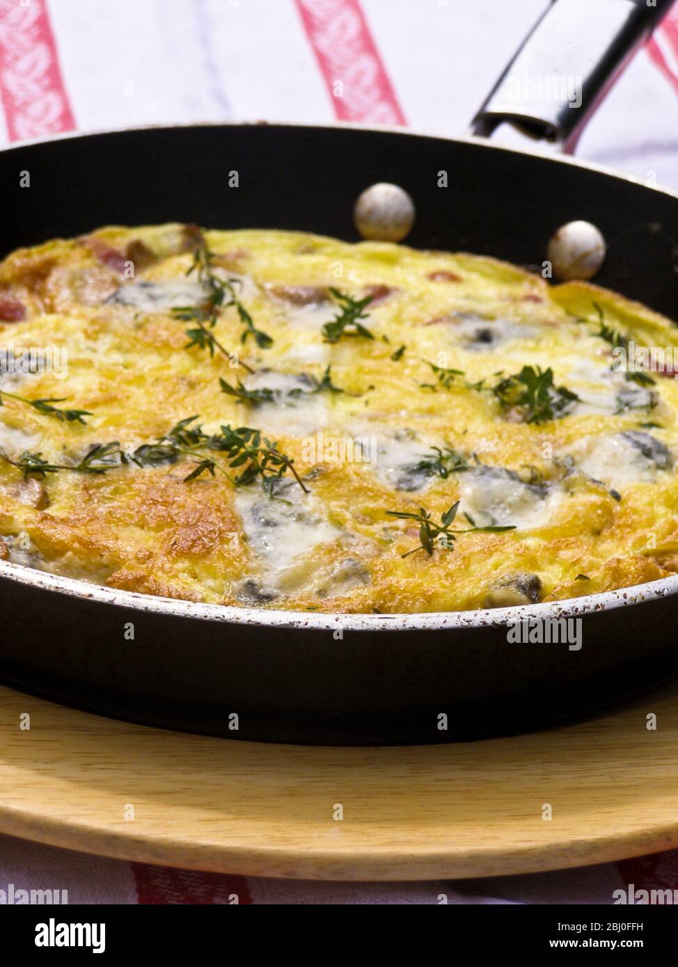 Frittata with goat's cheese, mushrooms and thyme, served in frying pan on wooden plate. - - Stock Photo