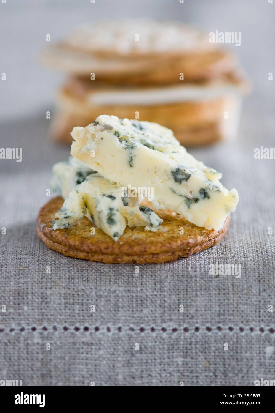 Stilton cheese on a wheat cracker on linen tablecloth. - Stock Photo